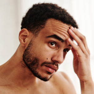 A thoughtful young man touching his forehead, representing the personal confidence that comes from healthy, hydrated skin.