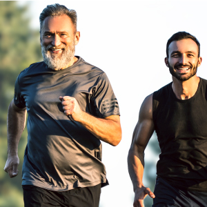 An older and a younger man smiling while jogging together, representing lifelong vitality and the importance of joint support for men's health.
