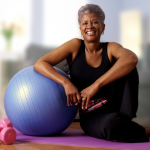 A smiling senior woman sitting with her exercise ball and weights, embodying a joyful and proactive approach to healthy aging and mobility.