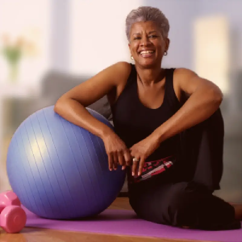 Active mature woman leaning on an exercise ball and smiling after a light workout.